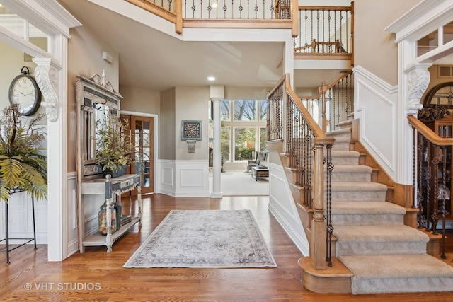 entrance foyer with a wainscoted wall, a decorative wall, a towering ceiling, wood finished floors, and ornate columns