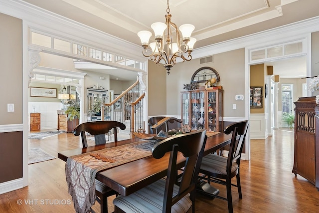 dining space featuring a wainscoted wall, visible vents, a tray ceiling, and wood finished floors