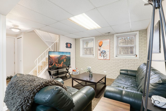 living room featuring brick wall and a drop ceiling