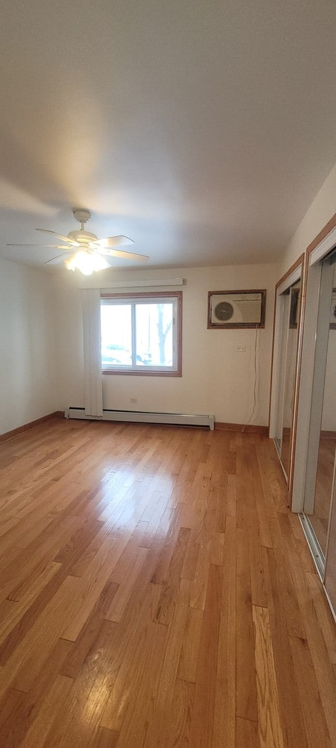 unfurnished room featuring a wall mounted air conditioner, light wood-type flooring, a baseboard radiator, and ceiling fan