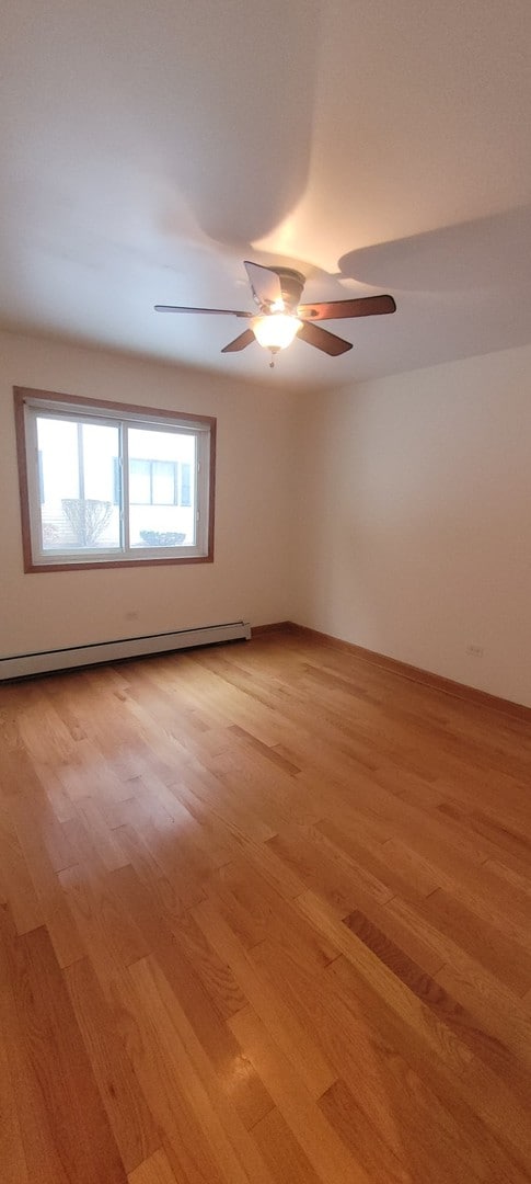 empty room with ceiling fan, light hardwood / wood-style floors, and a baseboard heating unit