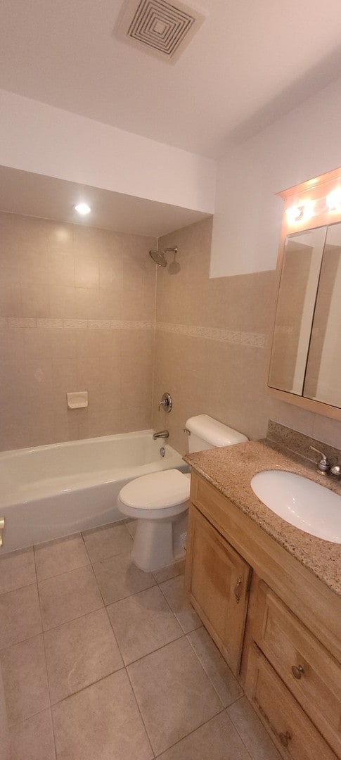 full bathroom with tile patterned floors, vanity, tiled shower / bath combo, and toilet