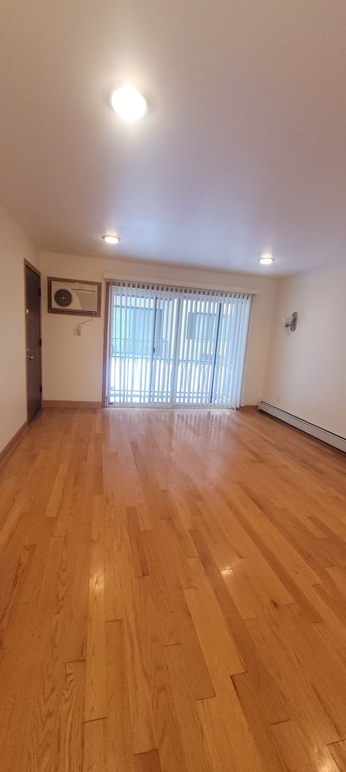 unfurnished room featuring a baseboard heating unit, a wealth of natural light, and light hardwood / wood-style flooring