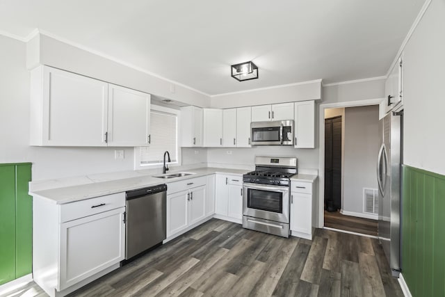 kitchen with light stone counters, ornamental molding, stainless steel appliances, sink, and white cabinetry