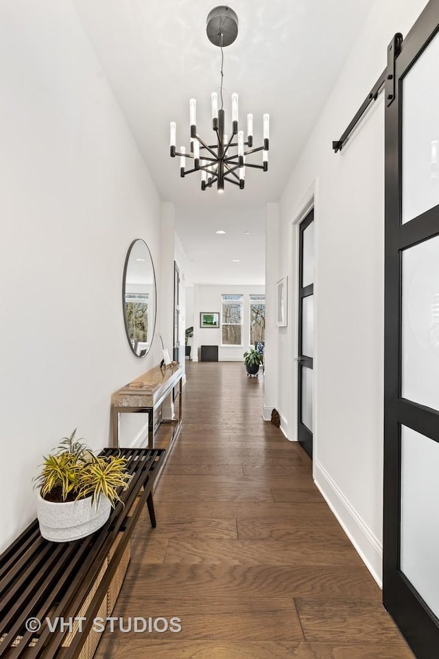 hall with a notable chandelier, a barn door, and dark wood-type flooring