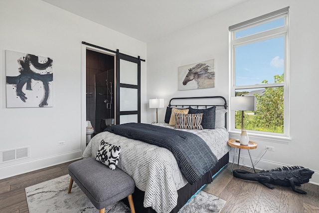 bedroom with a barn door, hardwood / wood-style flooring, and ensuite bath