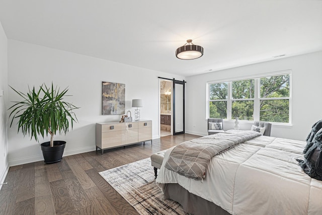 bedroom with ensuite bath, dark hardwood / wood-style flooring, and a barn door