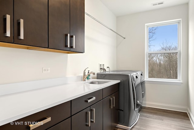 clothes washing area with hardwood / wood-style flooring, cabinets, independent washer and dryer, and sink