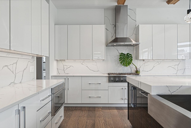 kitchen with white cabinetry, wall chimney range hood, light stone counters, pendant lighting, and stainless steel gas stovetop