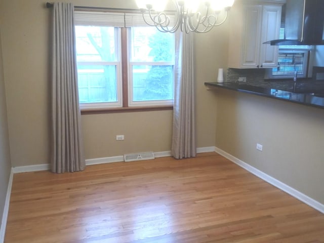 unfurnished dining area with light wood-type flooring, a notable chandelier, and sink