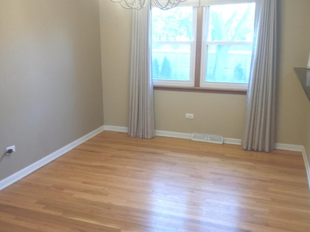 unfurnished room with plenty of natural light, a chandelier, and light hardwood / wood-style floors