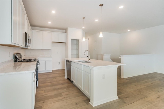 kitchen with white cabinets, appliances with stainless steel finishes, a kitchen island with sink, pendant lighting, and a sink