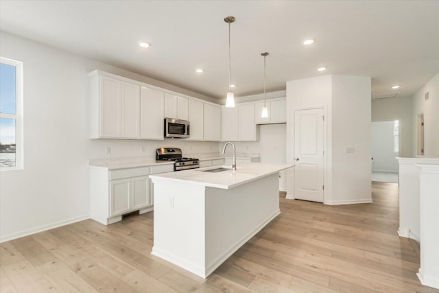 kitchen with a kitchen island with sink, stainless steel appliances, light countertops, white cabinetry, and a sink