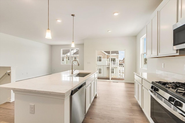 kitchen with appliances with stainless steel finishes, light stone counters, decorative light fixtures, a kitchen island with sink, and a sink