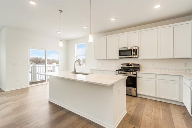 kitchen featuring a center island with sink, hanging light fixtures, appliances with stainless steel finishes, white cabinets, and light wood-type flooring