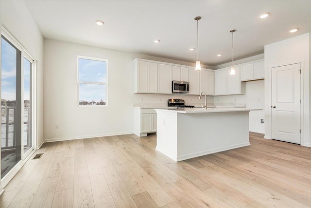 kitchen with an island with sink, stainless steel appliances, light countertops, white cabinetry, and pendant lighting