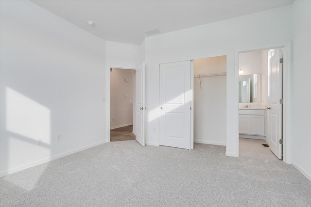 unfurnished bedroom with a closet, light colored carpet, baseboards, and ensuite bath