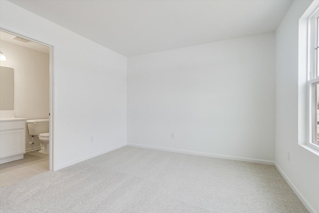 unfurnished bedroom with light carpet, ensuite bath, and baseboards