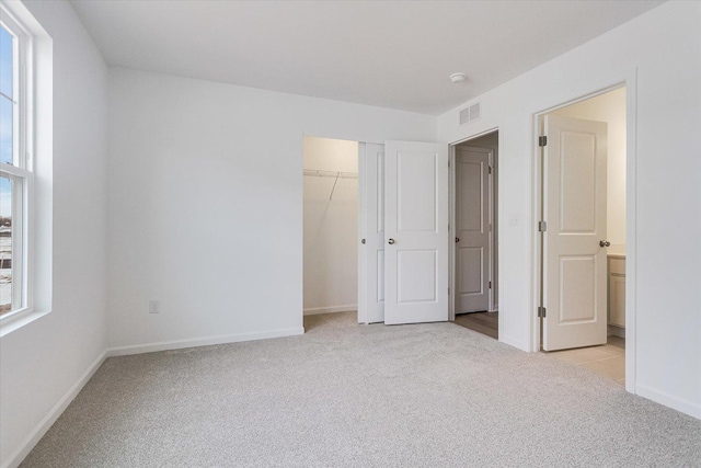 unfurnished bedroom featuring a closet, light colored carpet, visible vents, and baseboards