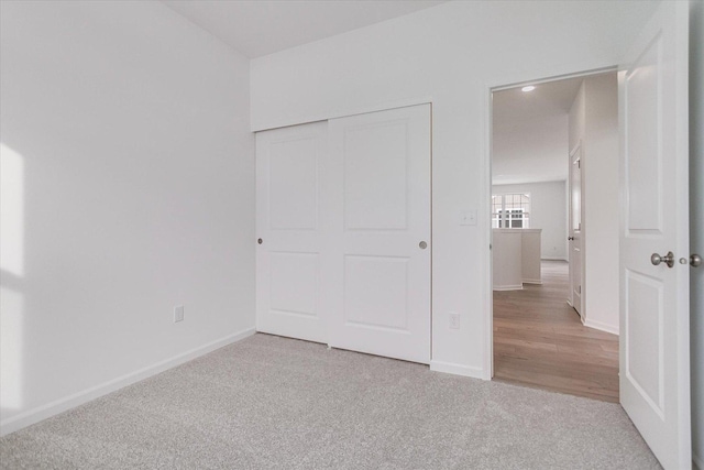 unfurnished bedroom with a closet, light carpet, and baseboards