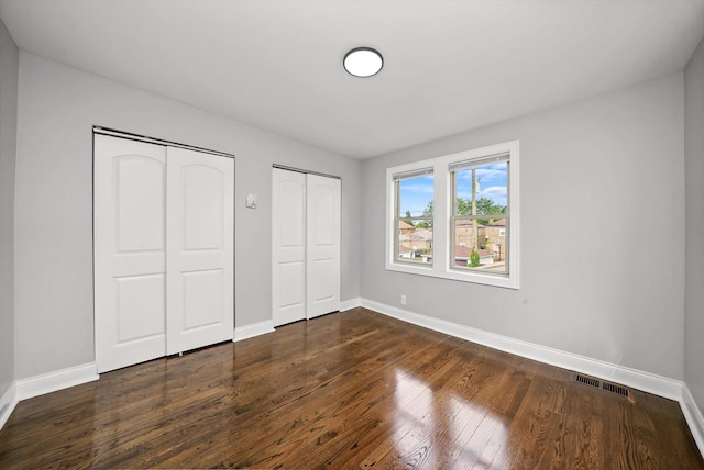 unfurnished bedroom with dark hardwood / wood-style floors and multiple closets