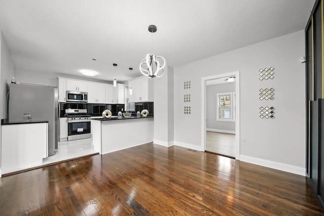 kitchen featuring stainless steel appliances, tasteful backsplash, kitchen peninsula, pendant lighting, and white cabinets