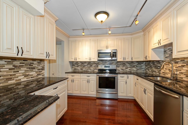 kitchen featuring dark stone countertops, sink, track lighting, and appliances with stainless steel finishes