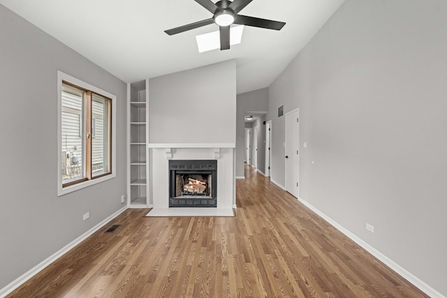 unfurnished living room featuring ceiling fan, a brick fireplace, built in features, lofted ceiling, and light wood-type flooring