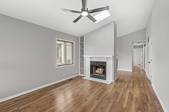 unfurnished living room featuring wood-type flooring, lofted ceiling with skylight, ceiling fan, and built in shelves