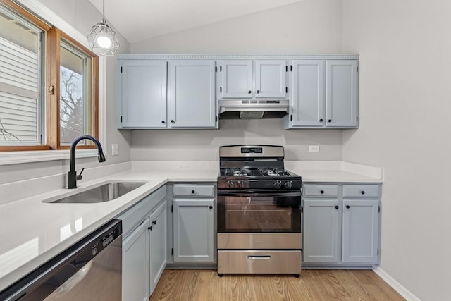 kitchen with appliances with stainless steel finishes, light wood-type flooring, vaulted ceiling, sink, and decorative light fixtures