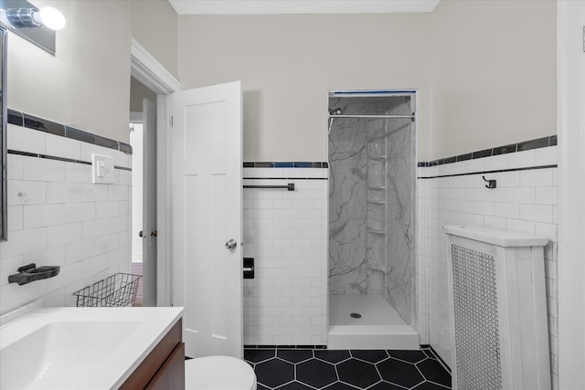 bathroom featuring a tile shower, tile walls, vanity, and toilet