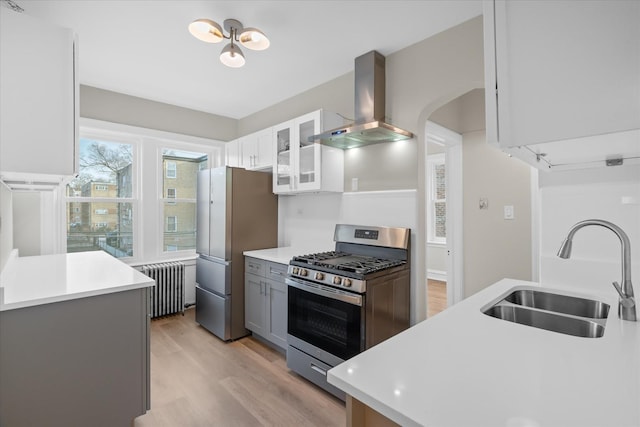 kitchen featuring extractor fan, appliances with stainless steel finishes, radiator heating unit, white cabinetry, and sink