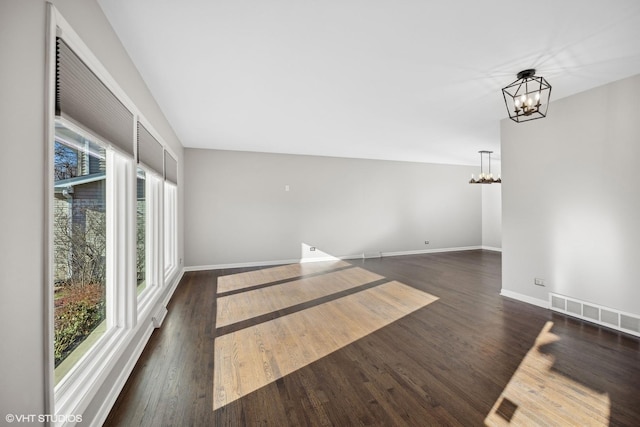 empty room featuring a notable chandelier and dark hardwood / wood-style flooring