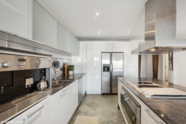 kitchen featuring dark stone countertops, island range hood, appliances with stainless steel finishes, sink, and white cabinetry