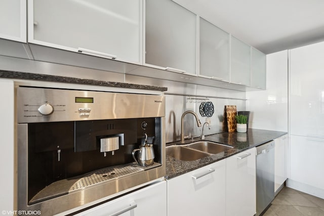 kitchen featuring stainless steel appliances, decorative backsplash, white cabinetry, dark stone counters, and sink