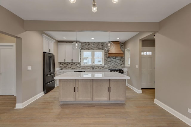 kitchen with a sink, a center island, custom exhaust hood, freestanding refrigerator, and decorative backsplash