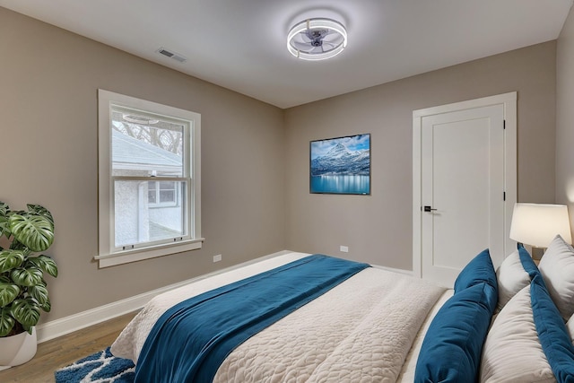 bedroom with baseboards, visible vents, and wood finished floors