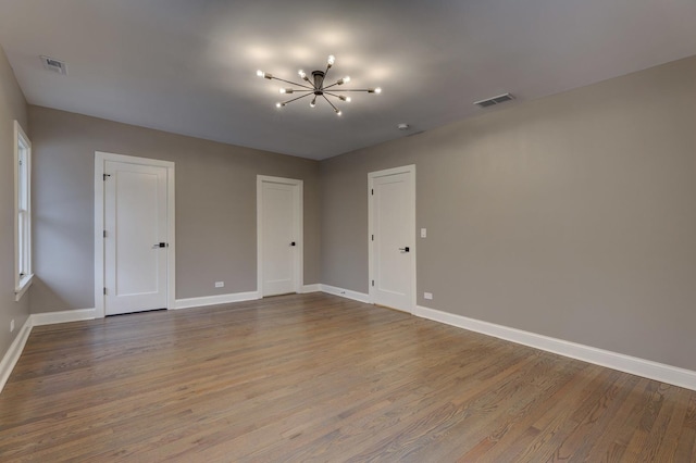 spare room with baseboards, wood finished floors, visible vents, and a notable chandelier