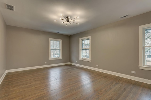 unfurnished room with a notable chandelier, dark wood-style flooring, visible vents, and baseboards