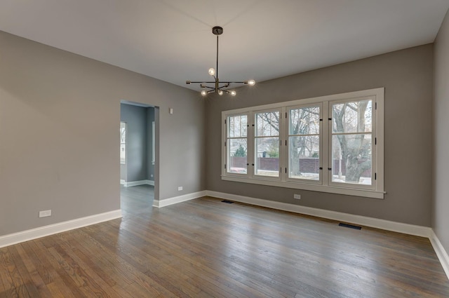 empty room featuring a notable chandelier, baseboards, visible vents, and wood finished floors