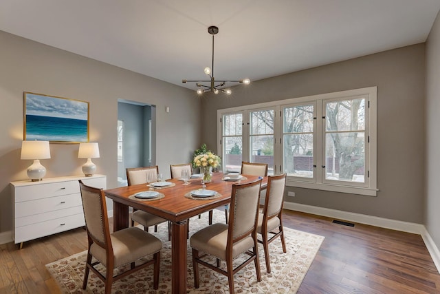 dining room featuring a notable chandelier, wood finished floors, visible vents, and baseboards