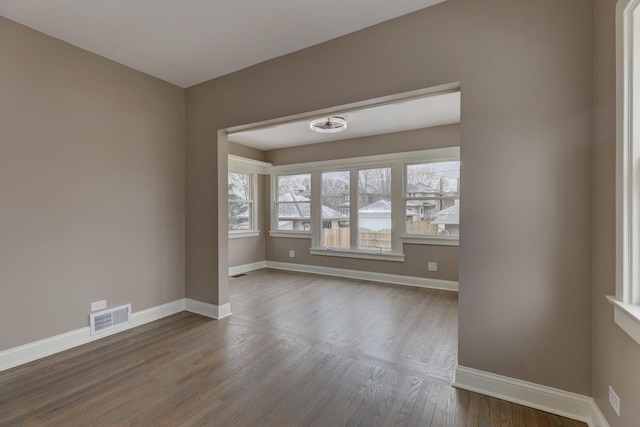 unfurnished room featuring dark wood-style floors, visible vents, and baseboards