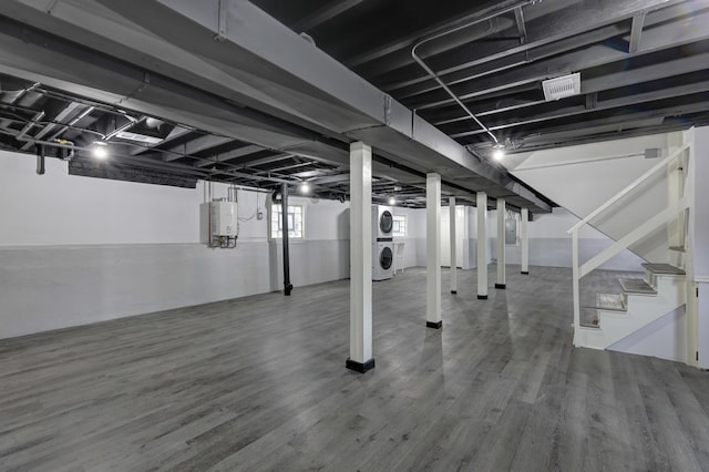 below grade area featuring stacked washer and clothes dryer, water heater, wood finished floors, electric panel, and stairs