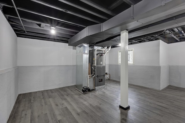 basement featuring a wainscoted wall, wood finished floors, and heating unit