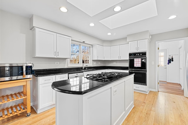 kitchen featuring a kitchen island, sink, white cabinets, black appliances, and light wood-type flooring