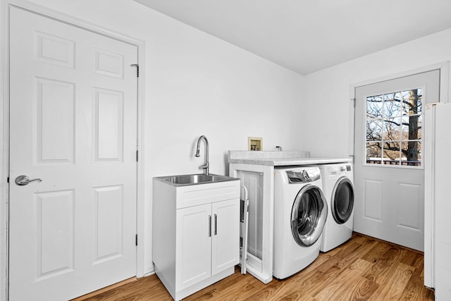 clothes washing area featuring cabinets, sink, washer and clothes dryer, and light hardwood / wood-style floors