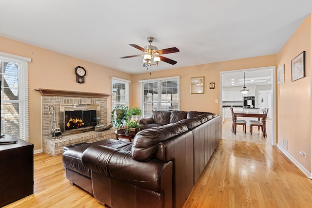 living room with ceiling fan, plenty of natural light, a fireplace, and light wood-type flooring