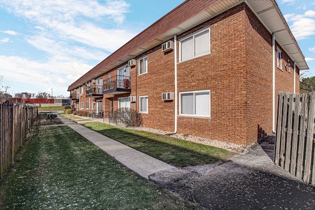 view of property exterior with a lawn, a balcony, and a wall mounted air conditioner