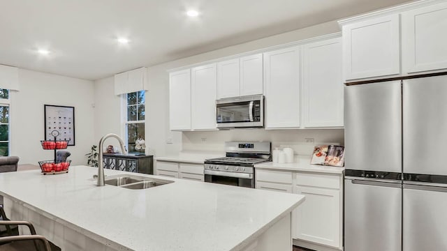 kitchen with a kitchen bar, white cabinetry, stainless steel appliances, sink, and a center island with sink