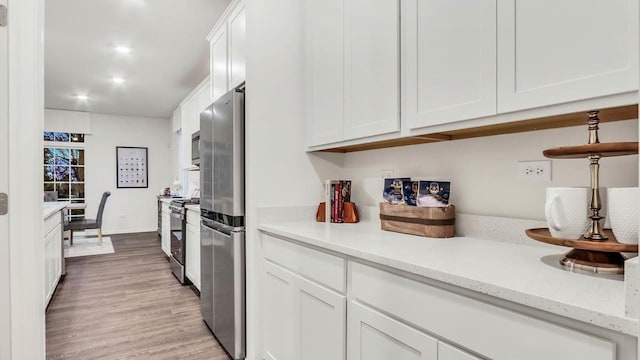 kitchen featuring white cabinetry, light hardwood / wood-style floors, stainless steel appliances, and light stone counters